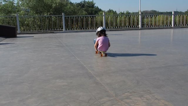 Little girl sitting on a skateboard. The child is riding on wheels.