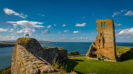 Wide angle shot of the medieval Scarborough Castle during sunset golden hour against a bright blue...