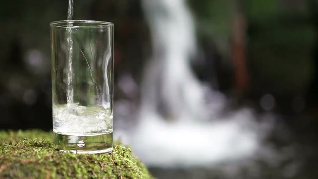 glass of fresh water with waterfall in the background
