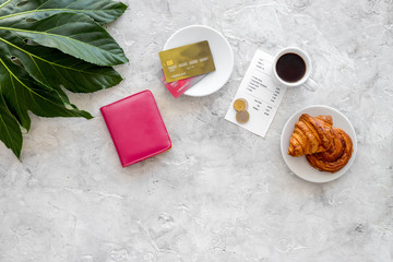Paying at cafe by card. Bill and coins near coffee, croissant and wallet on light stone table top view copyspace