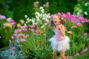 Fototapeta na wymiar happy little girl rejoices and jumps on a lawn near flowers, it is a lot of emotions