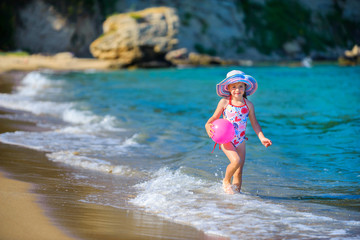 Obraz na płótnie Canvas happy little girl, plays in the coast, runs with a ball on waves