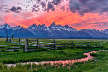 Sunset at Grand Teton - A panoramic view of a spectacular spring sunset at Teton Range, seen from an abandoned old ranch in Mormon Row historic district, in Grand Teton National Park, Wyoming, USA.  - obrazy, fototapety, plakaty