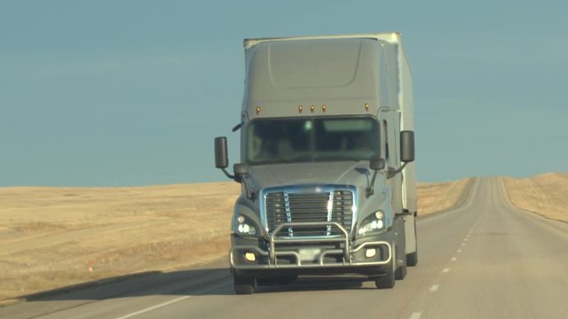 CLOSE UP: Unrecognizable grey semi truck driving directly into camera on empty highway across the Great Plains. Freight delivery truck transporting goods on interstate freeway. Trucking shipping cargo