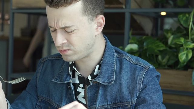 Stylish boy looks unhappy while eating unfresh salad in the cafe, steadycam shot

