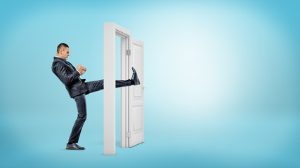 A businessman in side view kicks a small white door open with his leg on blue backgrounds.