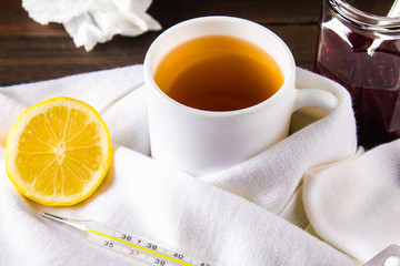 healthcare, traditional medicine and flu concept - cup of tea with lemon, thermometer and drugs on wooden table