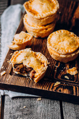 Fresh Traditional Australian meat mini pie on the wooden board on table background, closeup with copy space, top view, rustic style