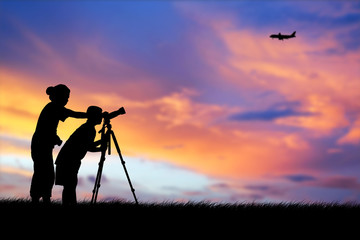 Silhouette of mother and son using camera shooting airplane during the sky sunset background