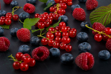 Black background with a set of red and blue berries with green leaves, raspberries and red currant