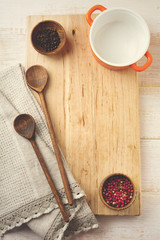 Black and red peppers, ceramic pan,  wooden stand, simple old spoons and  linen napkin on a light background. Kitchen accessories concept. Selective focus. Top view. Toned image.