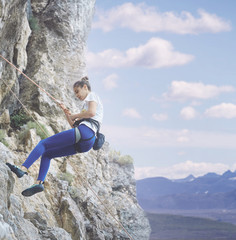 young cheerful woman climbs on the cliff. rock climber Learns to climb rocks on a rocky wall. woman makes hard move and looking up