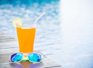Sunglasses with orange juice and a piece of lemon at the side of swimming pool. Vacation, beach, summer travel concept