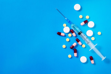 Medical preparations, pills and capsules and syringe lie on blue background. Copy space