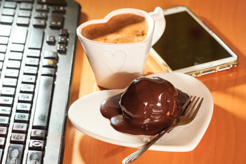 Cup of coffee and chocolate cake next to computer.