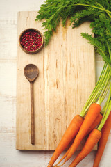 Black and red pepper, basil leaves, carrots,  ceramic pan,  wooden stand, simple old spoons and  linen napkin on  light background. Kitchen accessories concept. Selective focus. Top view. Toned image.