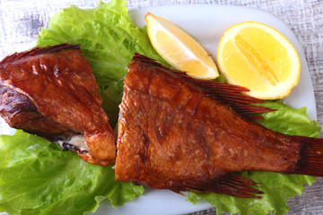 Smoked fish and lemon on green lettuce leaves on Wooden cutting board isolated on white background.