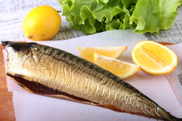 Smoked mackerele and lemon on green lettuce leaves on Wooden cutting board isolated on white background.