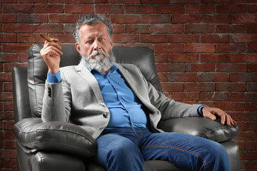 Handsome elderly man sitting in armchair with cigar