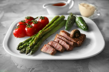 Sliced steak on white plate served with vegetables and sauce