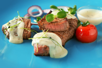 Sliced steak served with vegetables and white sauce on blue plate