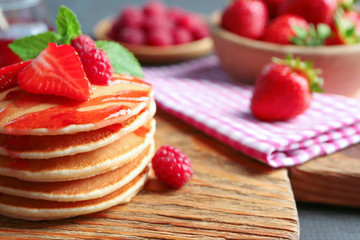 Delicious pancakes with raspberry and strawberry on wooden board