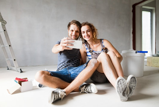Couple at home painting walls, taking selfie with smartphone.