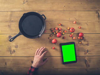 Over view of frying pan with tomatoes, tablet and hand