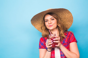 Sexy cute girl posing in studio, drinking fruit juice or cocktail on blue background and copy space