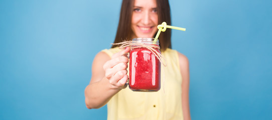 Beautiful young woman holding strawberry smoothie on blue background. Healthy organic drinks concept. People on a diet.