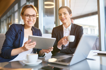 Group portrait of pretty coworkers looking at camera with charming smiles while having working meeting at spacious coffeehouse