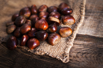 Ripe chestnuts on old wooden table and sack napkin close up with copy space. Roasted Chestnuts for Christmas.