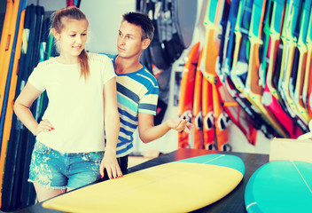 couple is choosing surfboard in nautical shop.