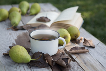 Hot tea, book, pear and autumn leaves on wood background.autumn relaxation concept