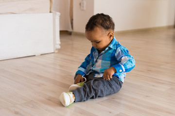 Naklejka premium Small child tries to put on his shoes. Mixed race baby boy with shoes