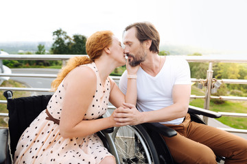 Nice wheelchaired couple kissing outdoors