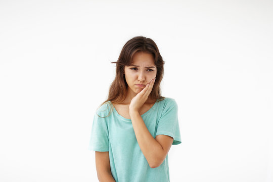 People, illness, sickness and health problems concept. Picture of unhappy young mixed race woman having sad painful expression on her face, suffering from bad toothache, holding hand on her cheek