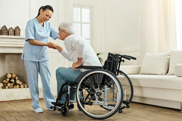 Joyful helpful caregiver holding her patients hand