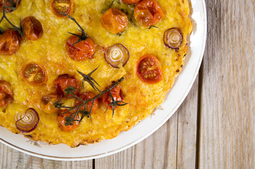 Rustic cake with cheese and cherry tomatoes on a wooden table.