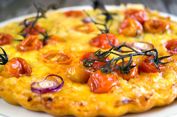 Rustic cake with cheese and cherry tomatoes on a wooden table.