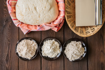 Homemade dough, sourdough in a jar, mix of flours, bread and basket for proof and spatula on a wooden background. Baking concept.