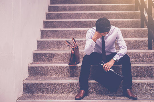 stressed businessman holding portfolio sitting at stairway. disappointed for job search