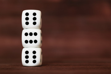Three white plastic dices on each other on brown wooden board background. Six sides cube with black dots. Devil's number 666.