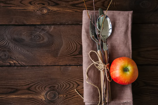 Tree branches, apple, cutlery on a linen sackcloth on a wooden background. Copy space and top view. Autumn mood, Halloween, Thanksgiving, Holiday concept.