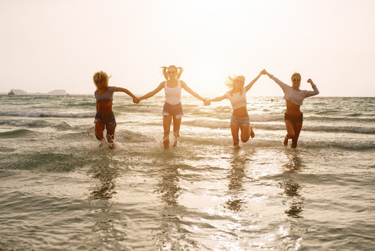 Four happy girls running in the sea and holding hands.