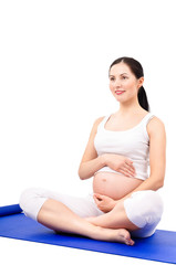 Beautiful pregnant woman sitting on a yoga mat, isolated on white background