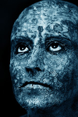 sad woman with damaged skin mask looking up in dark