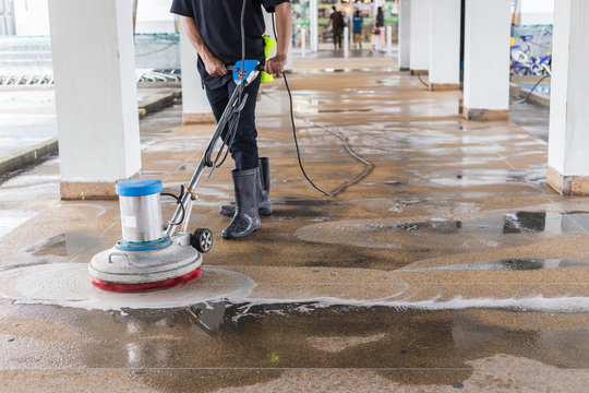 Worker cleaning sand wash exterior walkway using polishing machine and chemical or acid