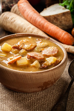 Wooden bowl of split pea soup with sausage and potatoes