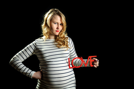 Young beautiful pregnant girl with blond curly hair holds LOVE sign at her belly, horizontal image